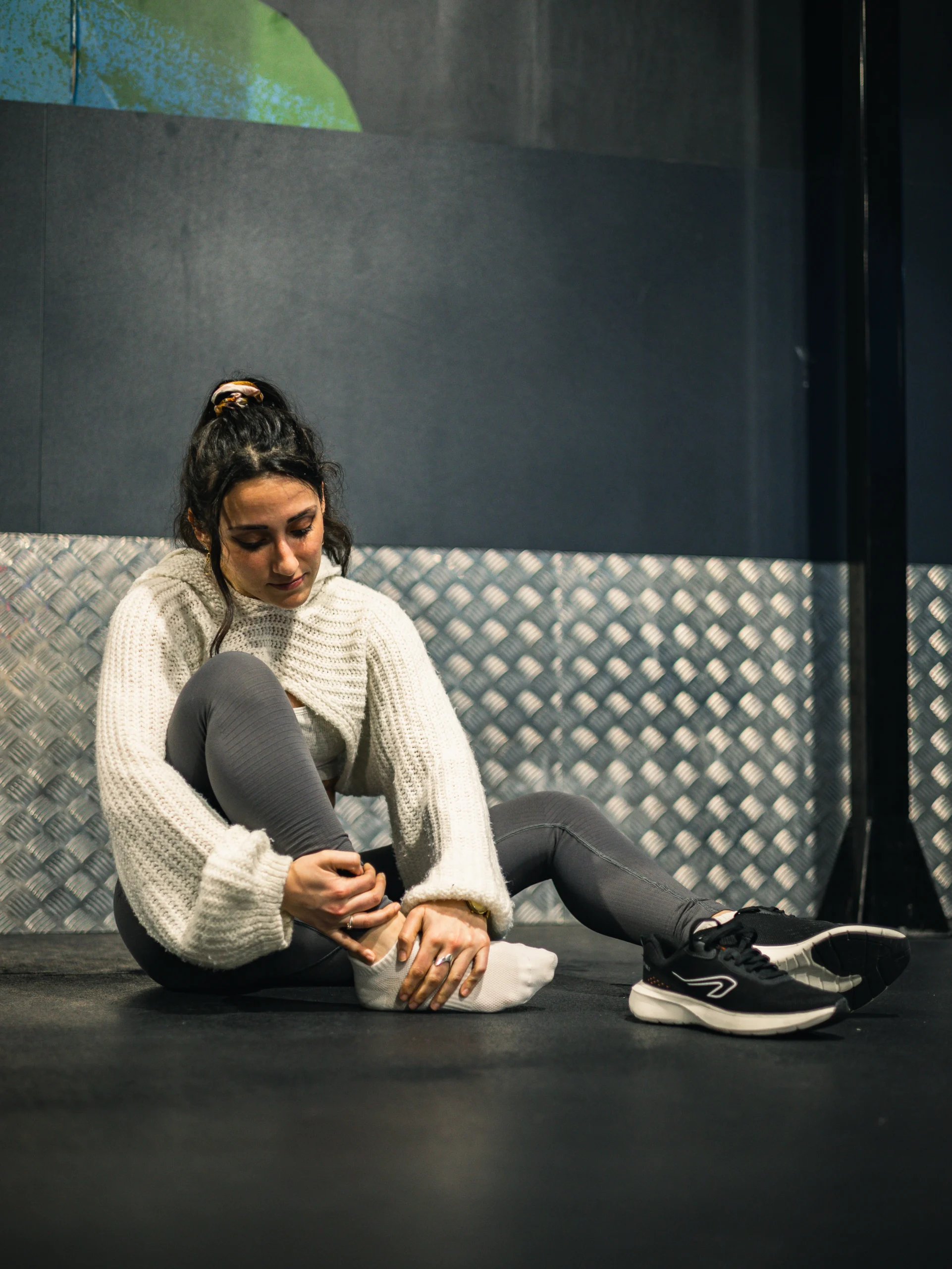 Sportive blessée tenant sa cheville en salle de sport, assise au sol après l’entraînement.